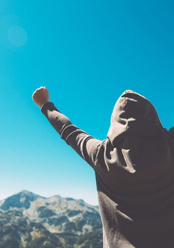 Winning and success. Victorious female person standing on mountain top with arms raised in V. Achievement and accomplishment in life. Toned image.